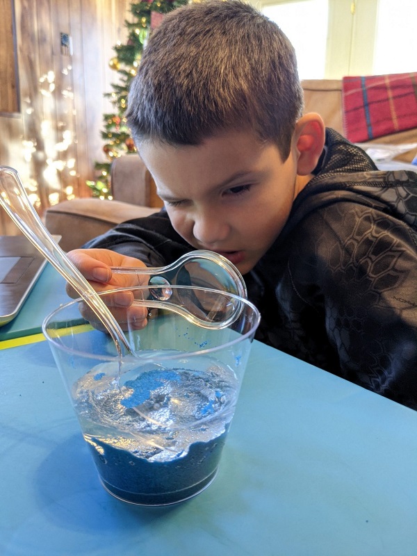 Boy with science experiment in cup and magnifying glass