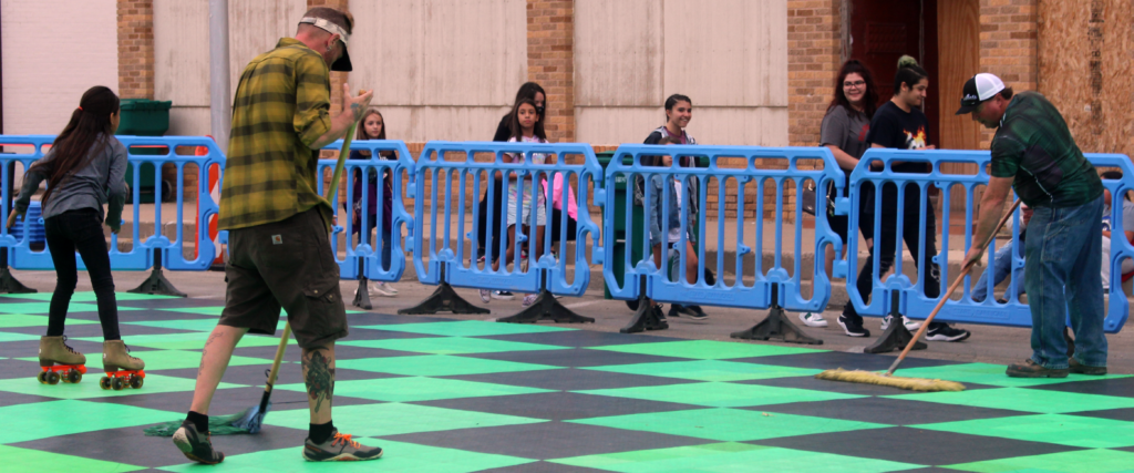 Two men mopping down a roller skating mat while a little girl skates nearby